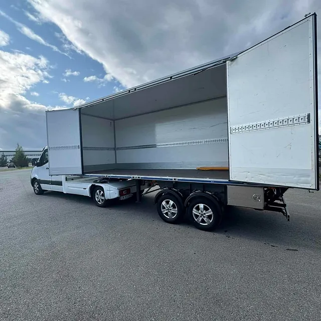 Åpen lastehenger med hvite sidevegger tilknyttet en lastebil, stående på asfalt.