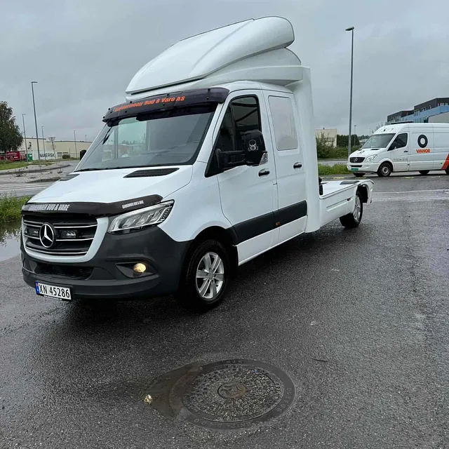 Hvit Mercedes skapbil uten lasteplan parkert på våt asfalt i gråvær.