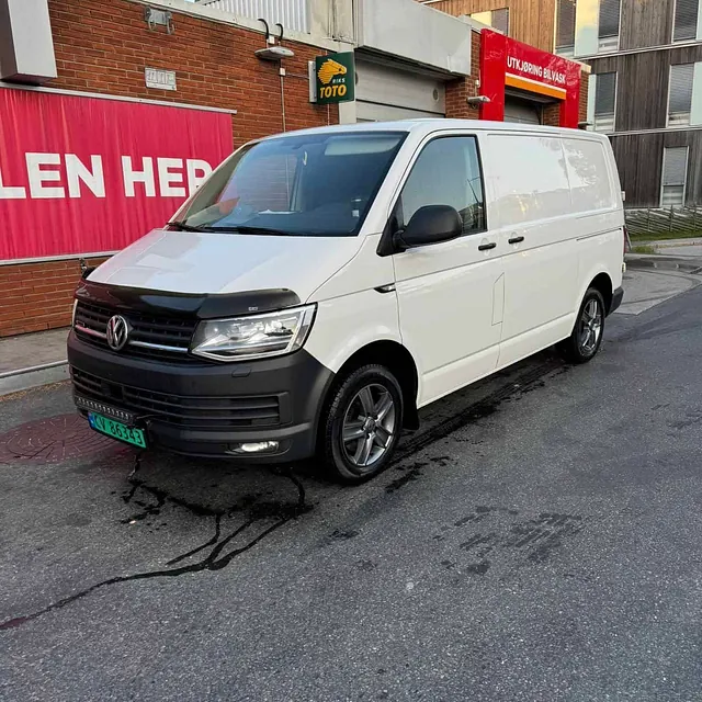 Hvit Volkswagen varebil parkert foran en bygning med røde skilt og skiltet "UTKJØRING BILVASK".