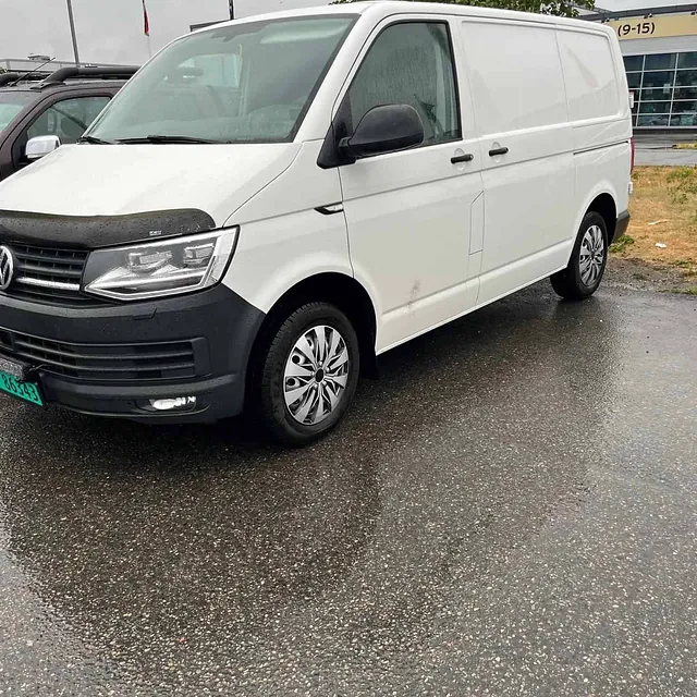 Hvit Volkswagen varebil parkert på våt asfalt en regnværsdag.